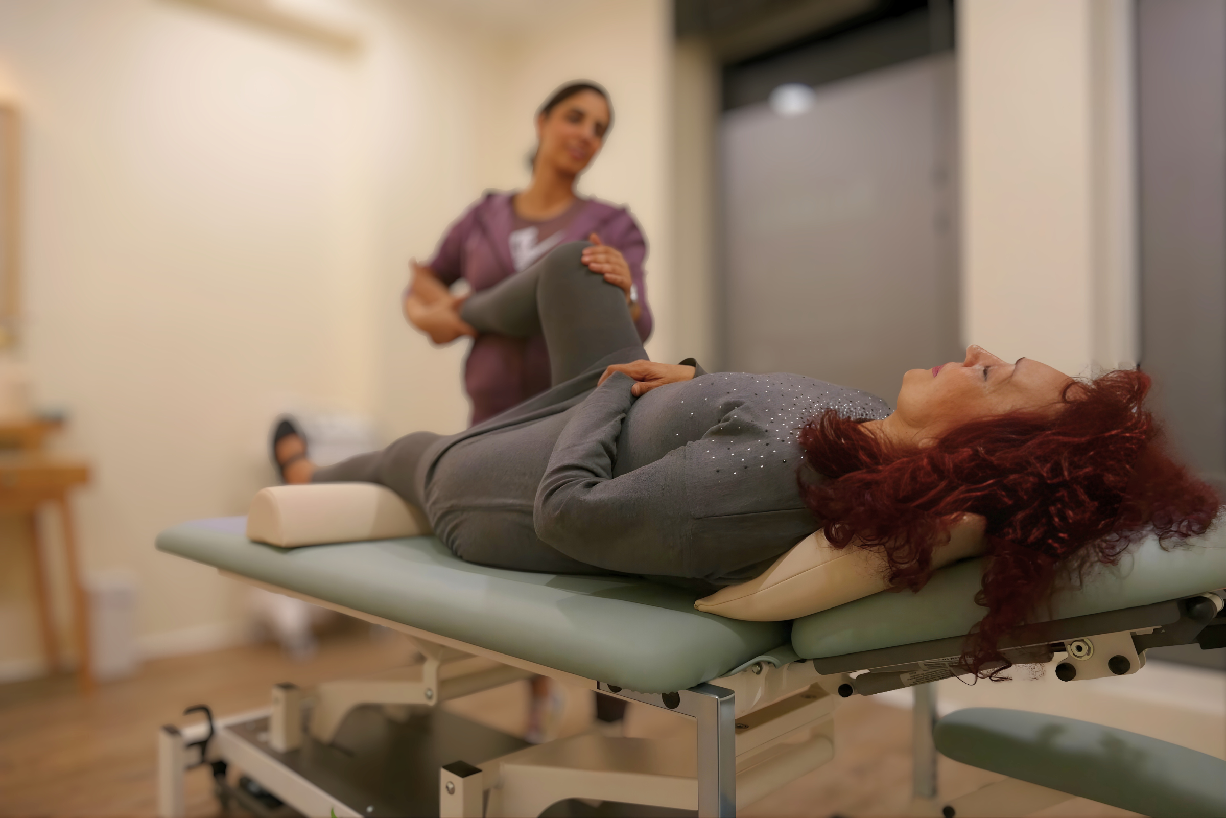 Physiotherapeutin führt eine manuelle Mobilisation des angewinkelten Knies einer entspannt liegenden Patientin auf einer Behandlungsliege durch.