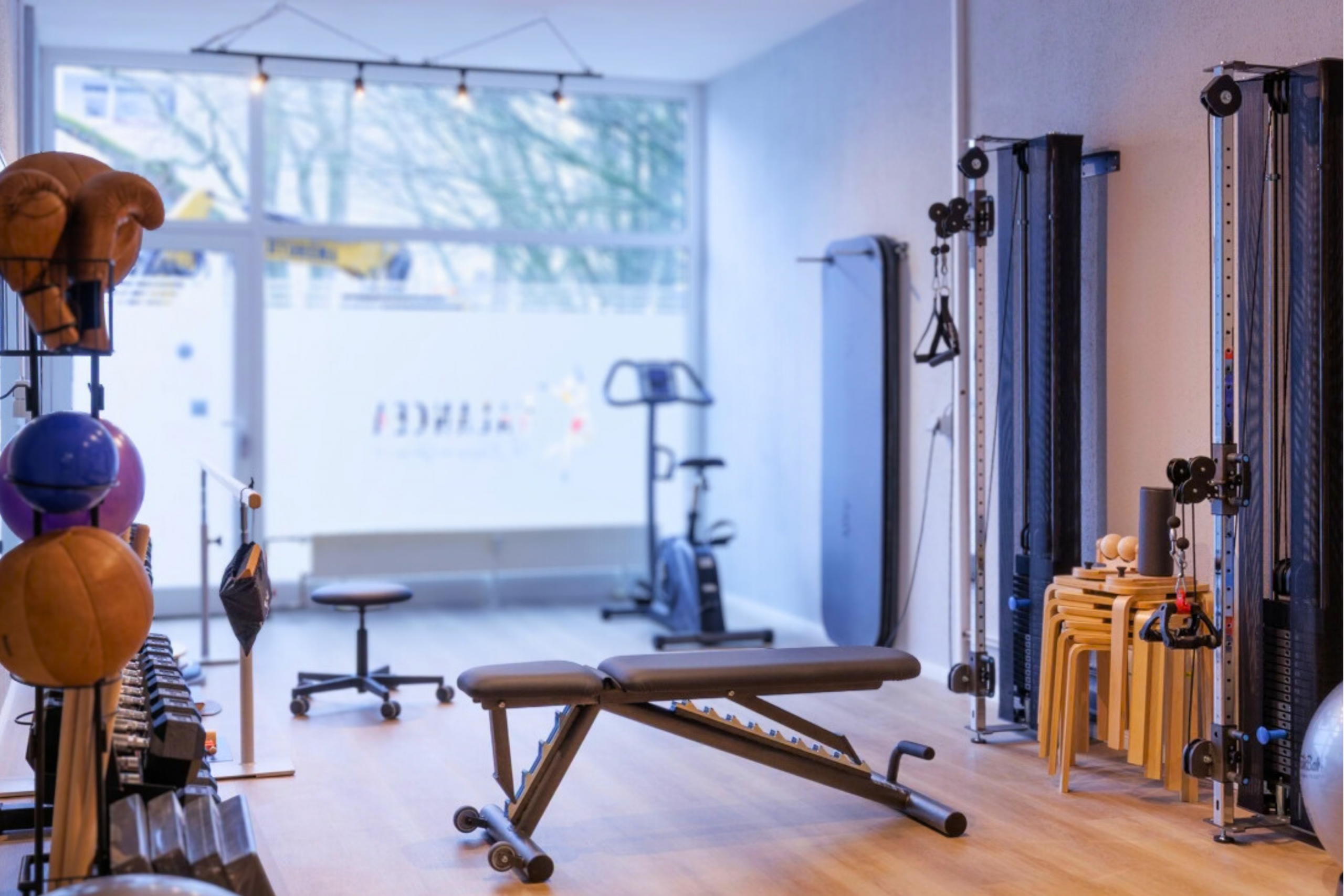 Heller Trainingsraum mit Trainingsbank, Seilzuggeräten, Kurzhanteln und Balance-Equipment in der Physiotherapiepraxis. Heller Trainingsraum mit Trainingsbank, Seilzuggeräten, Kurzhanteln und Balance-Equipment in der Physiotherapiepraxis.